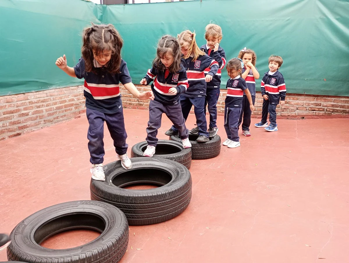 Chicos de Kinder cruzan un circuito de cubiertas en el patio del colegio
