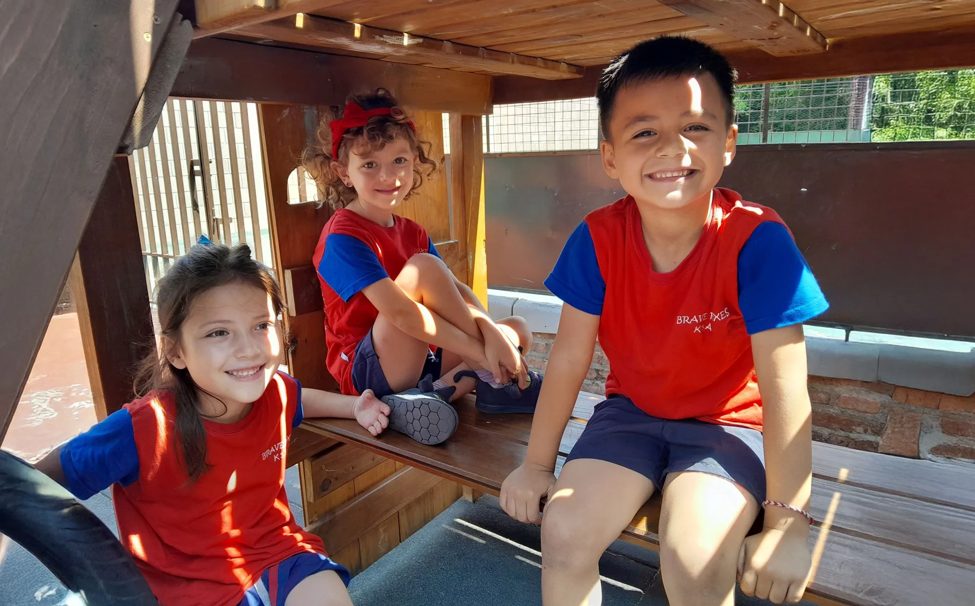 Tres chicos de Kinder sonríen desde el mangrullo de madera del patio