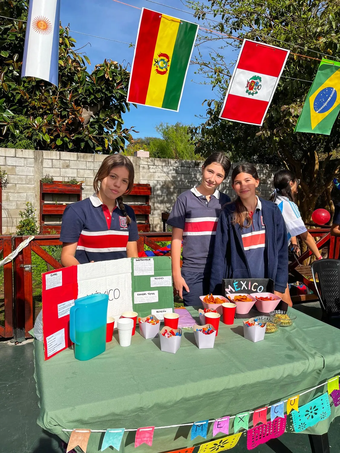Alumnas presentan su stand en la feria de idiomas, rodeadas de banderas